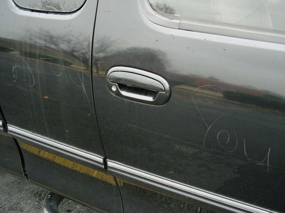 Dark truck door with scratches forming words, chrome handle, and trim