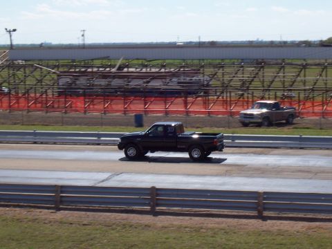2003 Ford Ranger - Two pickup trucks race on a drag strip with bleachers in the background.