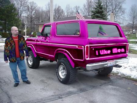 1978 Ford Bronco - A man stands beside a customized purple 1978 Ford Bronco with neon lettering on the tailgate.