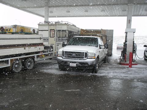 1989 Ford F-250 - A white Ford pickup truck is parked at a gas station with a trailer and RV during a snowfall.