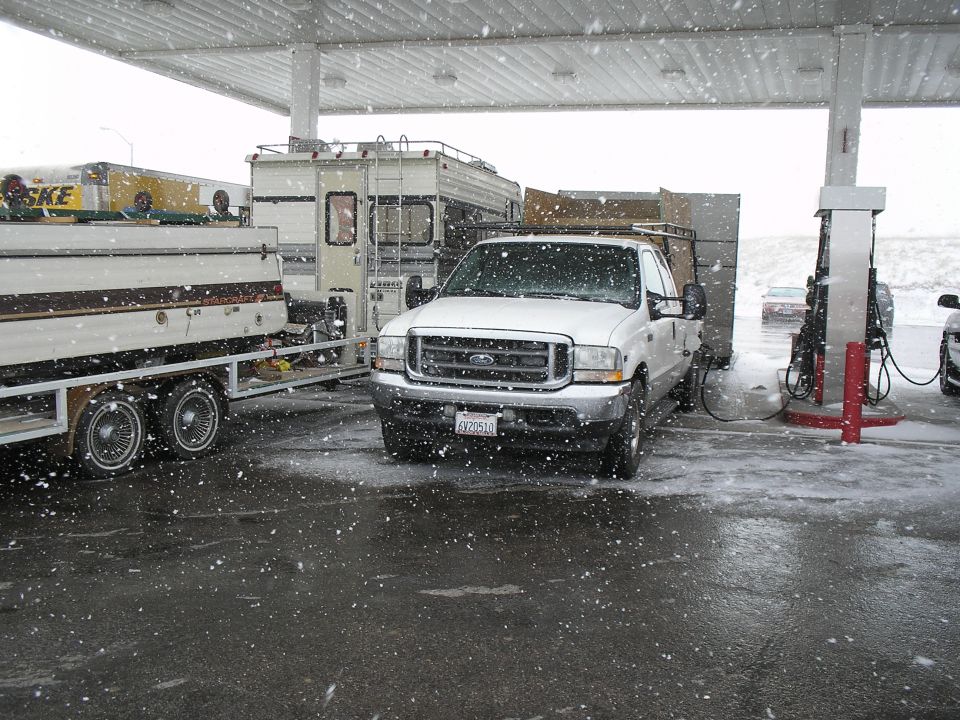 White Ford pickup truck with a trailer and RV at a gas station in the snow