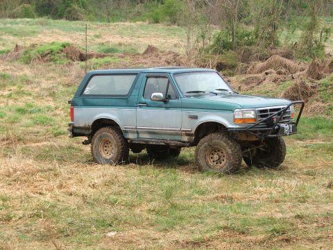 1996 Ford Bronco - A two-tone green and silver 1996 Ford Bronco sits in a grassy field with trees in the background.