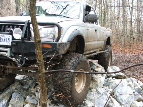 1996 Ford Bronco - This modified Toyota Tacoma is navigating a rocky trail in a wooded area.