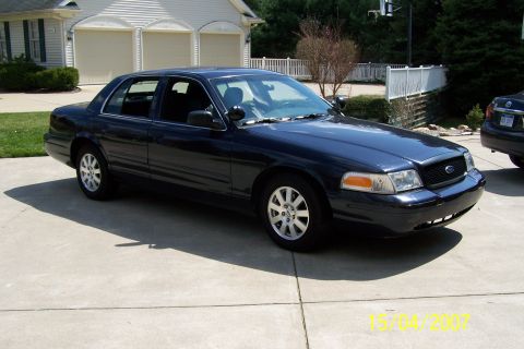2003 Ford Crown Victoria - A dark sedan is parked in a suburban driveway, with a house and another vehicle in the background.