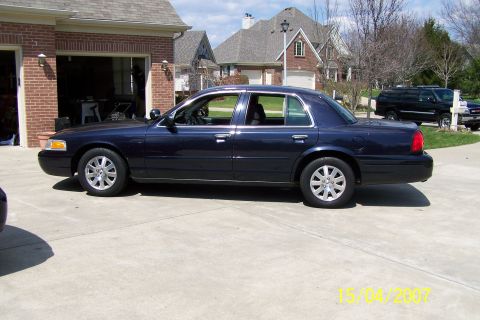 2003 Ford Crown Victoria - A dark blue 2003 Ford Crown Victoria is seen from the side in front of a brick garage.