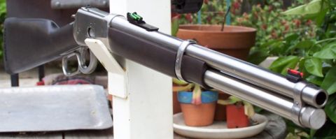 1990 Ford Bronco - A close-up view of a lever-action rifle, showing its metallic components and wooden stock against a blurred outdoor background.