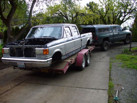 1978 Ford Bronco - A silver truck is loaded onto a trailer and towed by a green pickup truck.