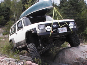 1996 Ford Bronco - Off-road Jeep Cherokee XJ navigating rocky terrain with a canoe secured on top.