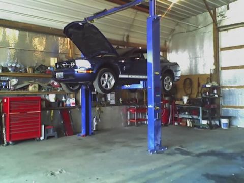 1992 Ford Bronco - A blue Ford Mustang is raised on a hydraulic lift inside a workshop, with its hood open.