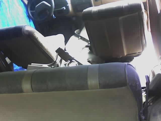 Interior of a Ford Bronco seen from rear seat, showing folded front seats, steering wheel, and blue tarp on left side