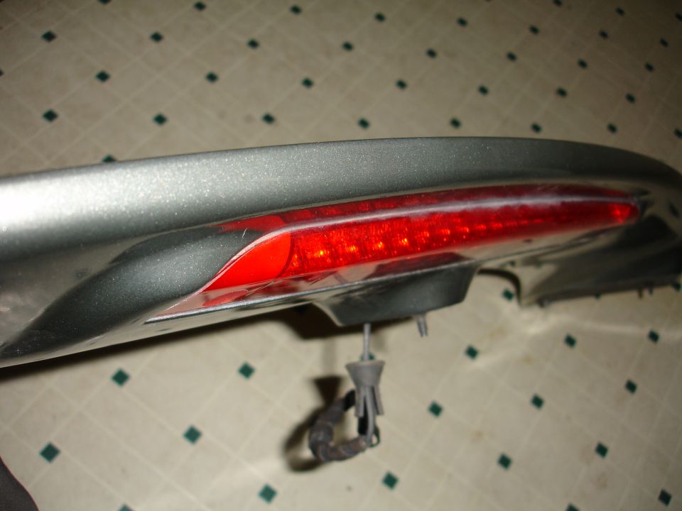 Silver car spoiler with a red LED brake light strip. A gray connector hangs below