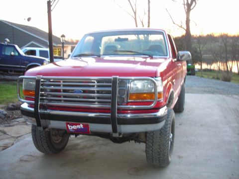 1995 Ford F-250 - A red Ford F-250 pickup truck is parked outside with a lake in the background.