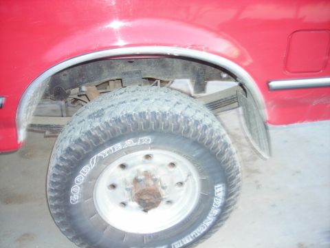 1995 Ford F-250 - Close-up of the rear wheel assembly of a red truck, revealing suspension components and tire details.