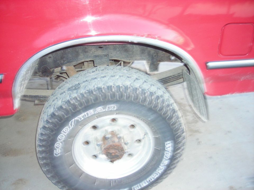 Red truck rear wheel with Goodyear Wrangler tires, showing leaf springs and fender flare