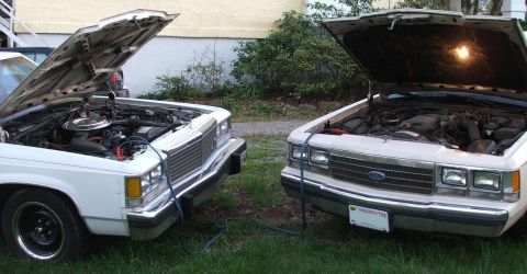 1991 Ford Crown Victoria LTD - Two Ford Crown Victorias hooked up with jumper cables in a grassy yard.