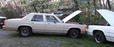 1991 Ford Crown Victoria LTD - A tan 1991 Ford Crown Victoria LTD sedan is parked next to another vehicle with its hood open.