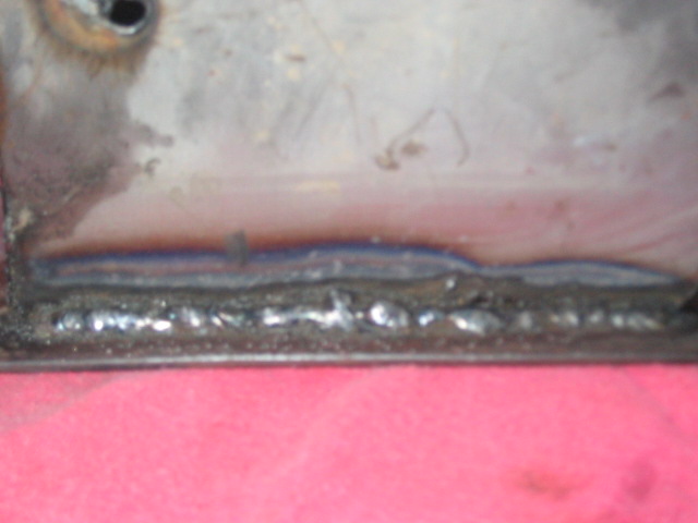 Close-up of a rough metal weld seam on a piece of metal, with a pink surface below