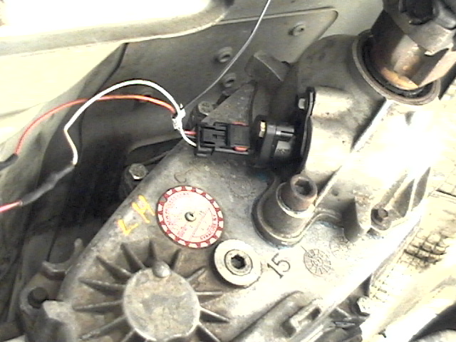 Transfer case sensor with white and orange wires connected to a black connector. Part of a vehicle's drivetrain