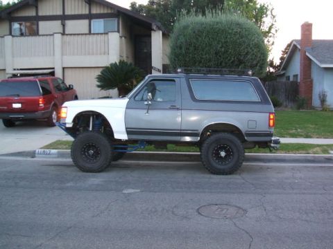 1988 Ford Bronco - This modified Ford Bronco is parked in front of a house, with another SUV visible in the driveway.
