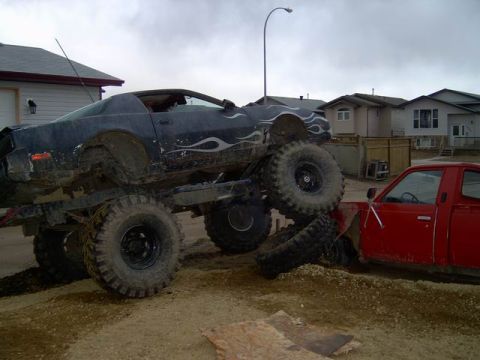 1995 Ford Bronco - A modified monster truck with flame decals is perched precariously on top of a red pickup truck.