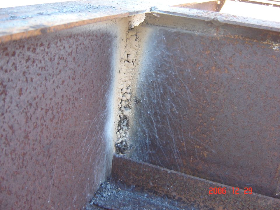 Welded metal corner with rust and slag, showing a date stamp of 2006