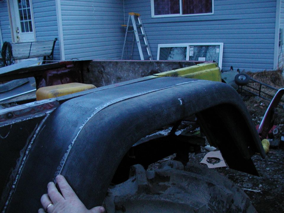 Dark fender and bed of a disassembled vehicle, with a yellow container visible
