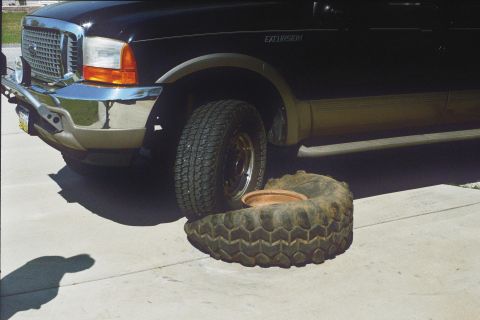 1978 Ford Bronco - Ford Excursion with a flat tire on the ground next to it.