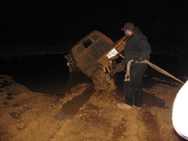2005 Ford Excursion - A man is winching a stuck, old truck out of the mud at night.