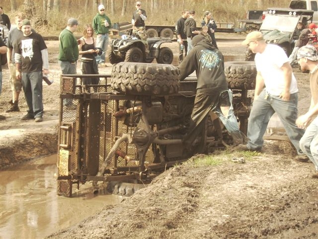 off-road vehicle flipped over in mud pit with people around