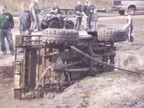 1987 Suzuki Samurai - An overturned vehicle lies in a muddy pit, surrounded by onlookers and other vehicles.