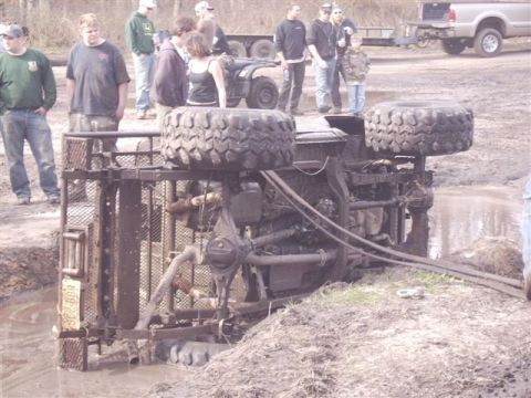 1987 Suzuki Samurai - An overturned off-road vehicle lies in the mud while onlookers observe the scene.
