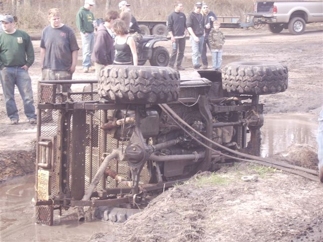 Overturned off-road vehicle in mud with people watching