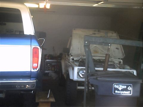 1978 Ford Bronco - Two vehicles are parked inside a garage, one is a white Suzuki Samurai with its hood up.