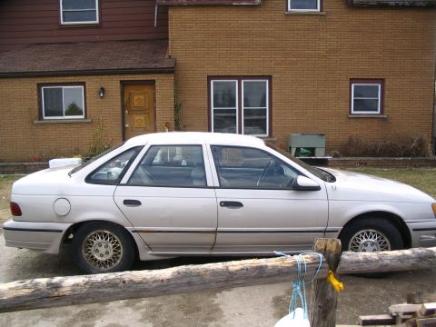 1993 Ford Taurus - A light-colored 1989 Ford Taurus sedan is parked in front of a brick house.