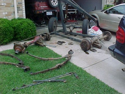 1978 Ford Bronco - Vehicle axles and leaf springs are disassembled and spread across the driveway and lawn.