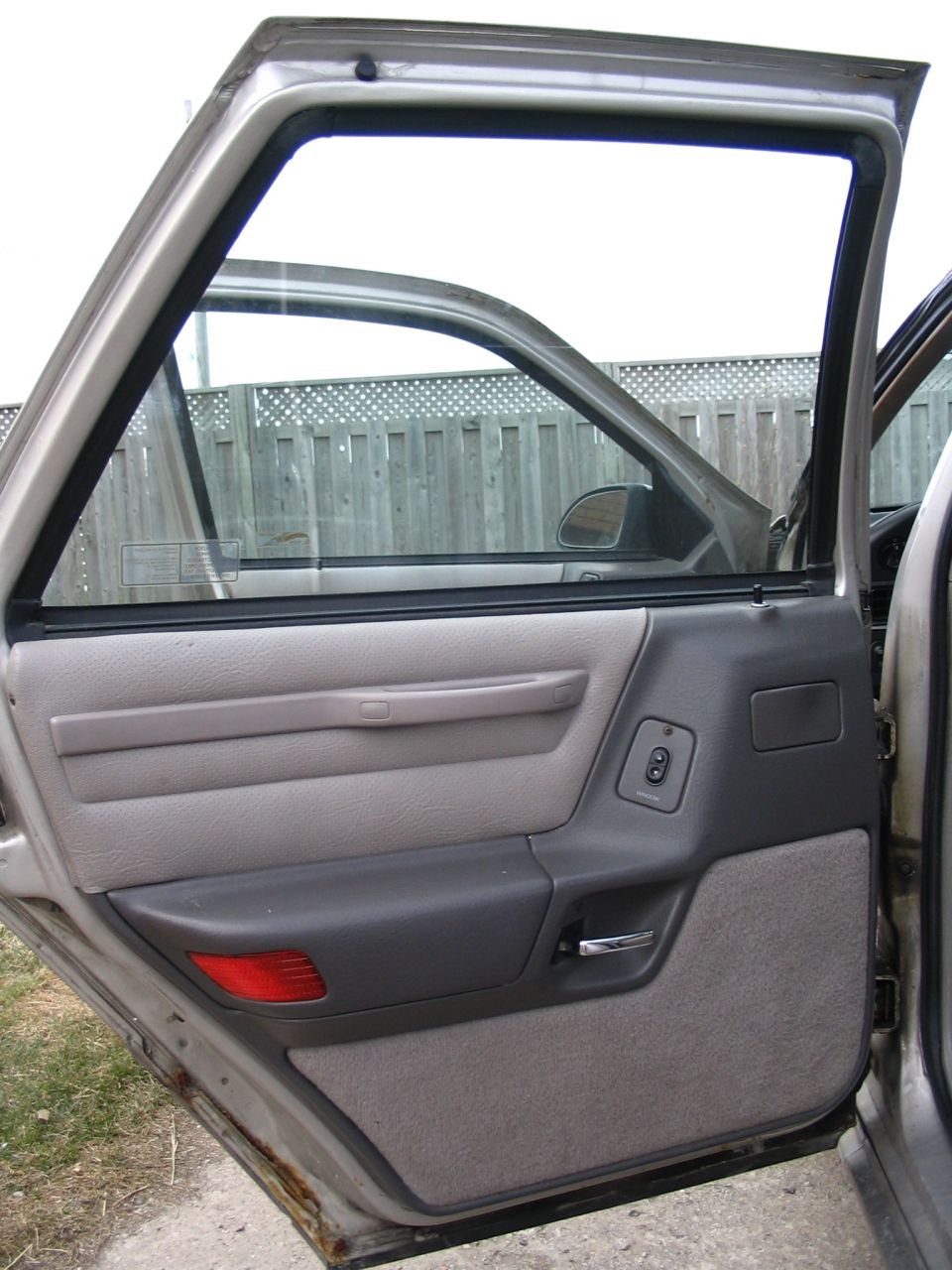 1989 Ford Taurus interior door panel with gray fabric and dark gray plastic trim, showing a red reflector and window controls