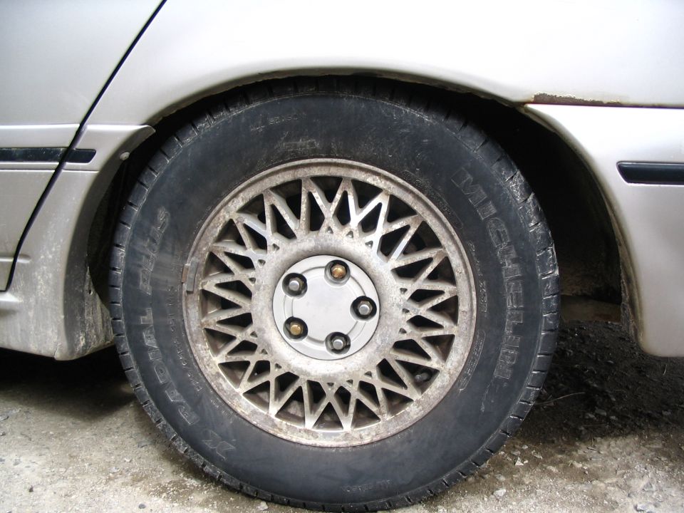 Silver wheel with intricate spokes on a silver car. Tire has visible text