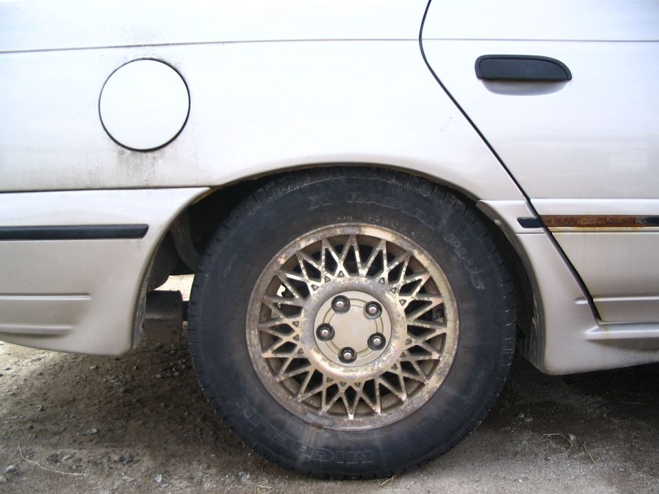 Rear wheel and fender of a car, showing a gas cap door and a wire-spoke wheel