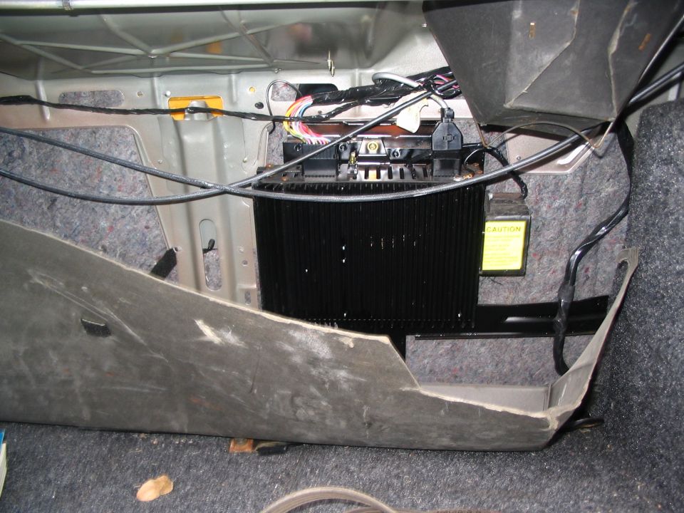 Car trunk interior with exposed wiring and a black amplifier unit, viewed from above