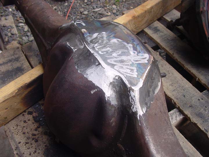Close-up of a rusty differential housing with a welded patch on top. Some white markings are visible on the patch