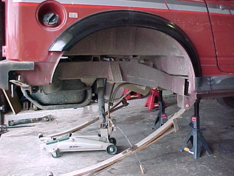 1978 Ford Bronco - The rear suspension of a red SUV is elevated on jack stands for maintenance, with a floor jack positioned below.