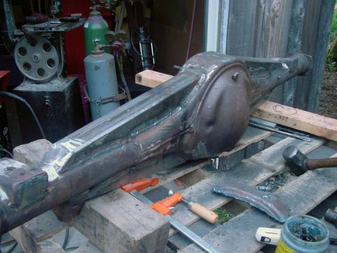 1979 Ford Bronco - A rusty rear axle housing sits on wooden blocks, surrounded by tools like hammers and clamps.