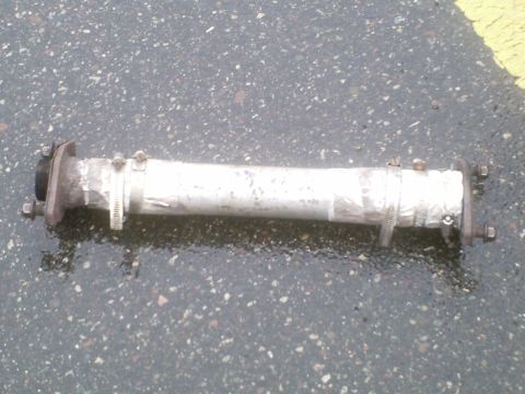 1995 Ford Probe - A section of exhaust pipe with flanges and clamps is shown lying on a wet asphalt surface.
