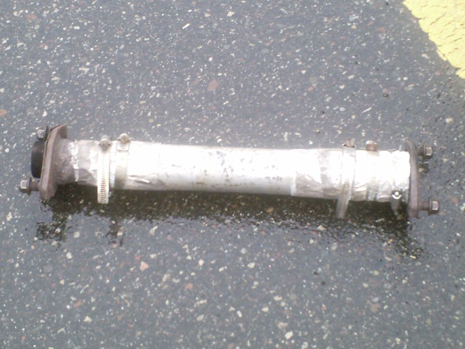 Exhaust pipe section patched with aluminum tape and hose clamps, lying on asphalt