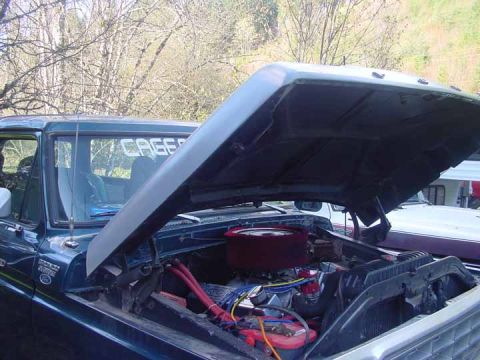 1979 Ford Bronco - The engine bay of a dark blue truck is visible with the hood open. Text reading 'CAGE' is present on the windshield.