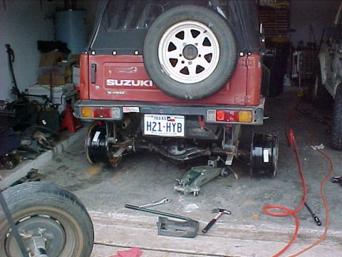 1978 Ford Bronco - The rear of a red Suzuki Samurai is shown with its wheels removed, indicating it is being worked on in a garage.