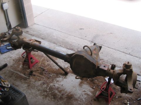 1991 Ford Bronco - Front axle assembly, likely from a truck or SUV, is disassembled and resting on jack stands in a garage.