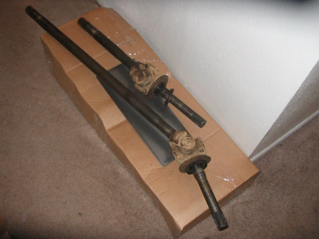 Two Dana 60 front axle shafts with U-joints, resting on cardboard