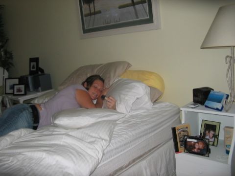 1991 Ford Bronco - A woman rests on a bed in a bedroom, with a lamp and framed photos nearby.
