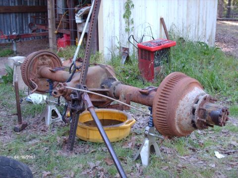 1990 Ford F-150 - A rusty rear axle assembly is supported by jack stands, with a yellow oil pan beneath it, suggesting maintenance or repair work.